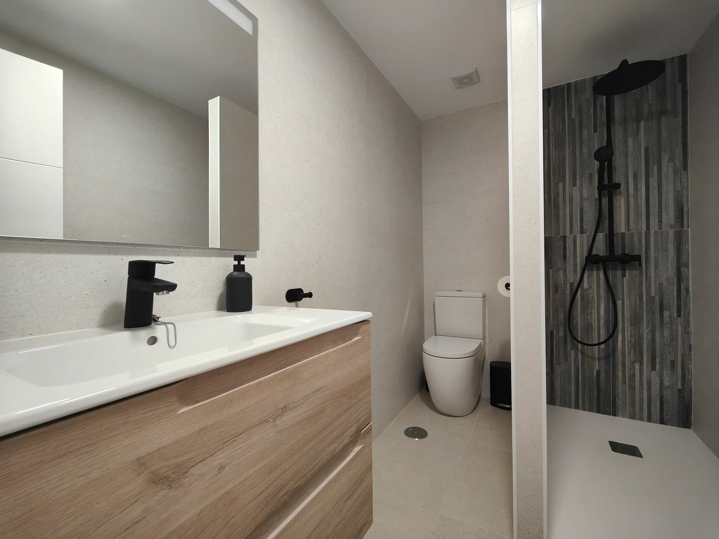 Baño reformado con lavabo, mueble de madera y ducha